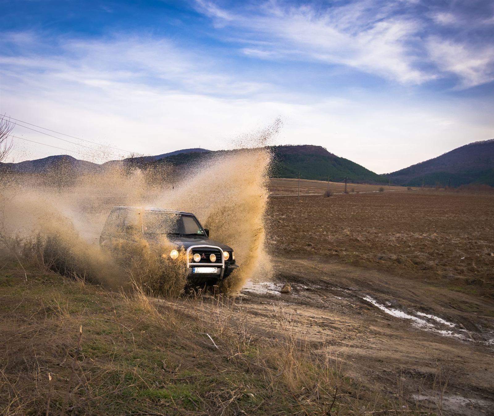 Un 4×4 traverse un chemin de terre en projetant de la boue