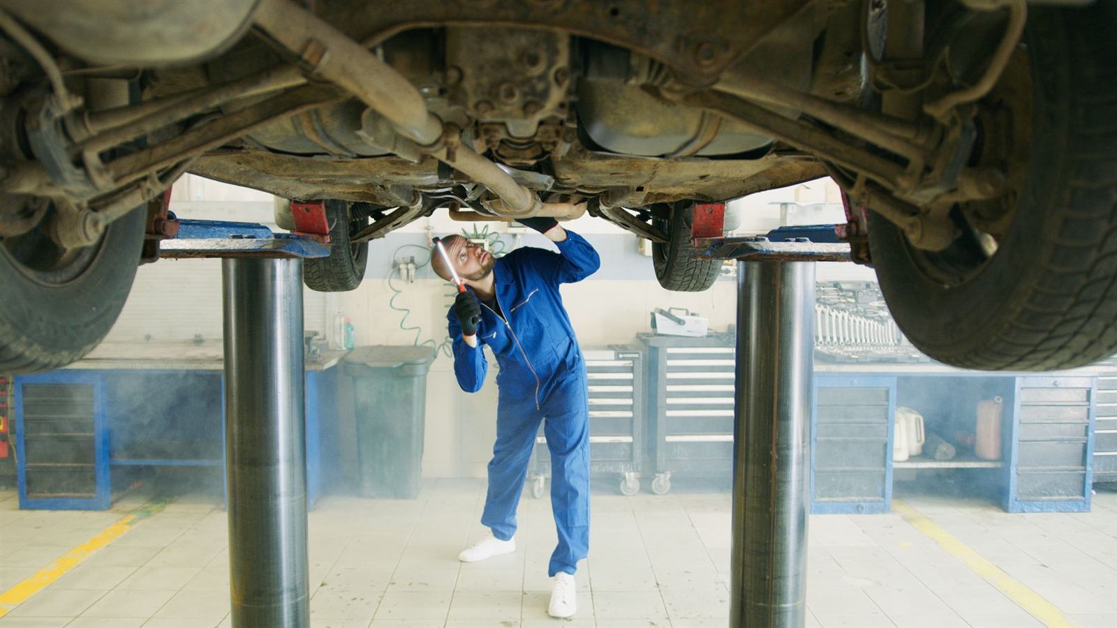 Un contrôleur en bleu de travail inspecte le dessous d'un véhicule sur un pont élévateur